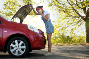 Woman looks under the hood of her lemon car on the side of the road in California